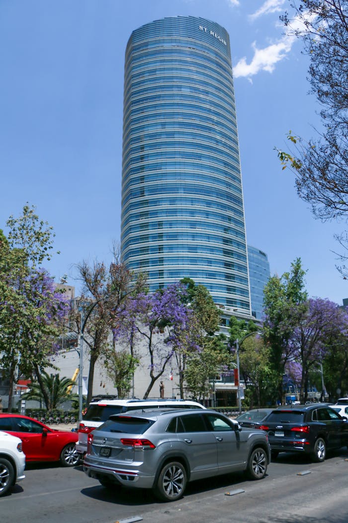 St. Regis Hotel skyscraper in bustling Mexico City, surrounded by traffic and trees.